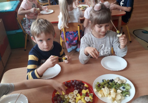 Dzieci nakładają kawałki owoców na patyczki