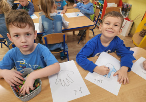 Jaś.L i Adaś.G malują kontur swojej rączki.