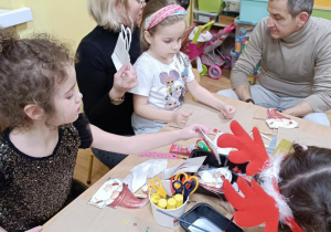 Dzieci z rodzicami ozdabiają torebki na prezenty.