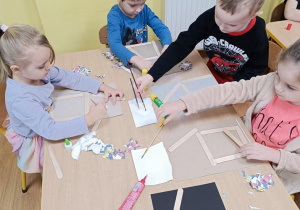 Dzieci wykonują karmnik z patyczków higienicznych, wycinają i doklejają w odpowiednich miejscach ptaki.