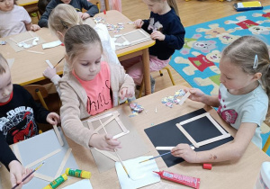 Dzieci wykonują karmnik z patyczków higienicznych, wycinają i doklejają w odpowiednich miejscach ptaki.