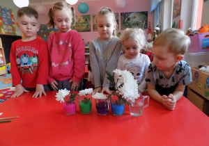 Filip, Zosia, Patrycja, Asia i Tymek prezentują swoje kwiatki w kolorowej wodzie.