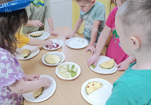 Dzieci układają dinusie z ananasa, mango, granatu i kiwi.