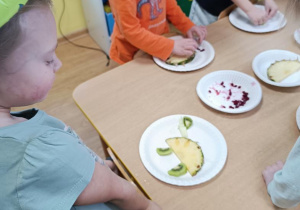 Dzieci układają dinusie z ananasa, mango, granatu i kiwi