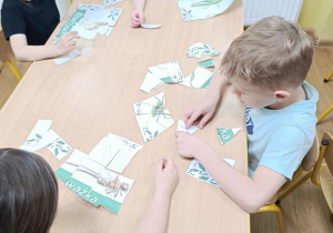 Dzieci składają puzzle ze zwierzętami zamieszkującymi łąkę.