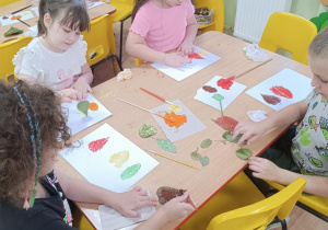 Dzieci stemplują liście tworząc z nich jesienne drzewa.