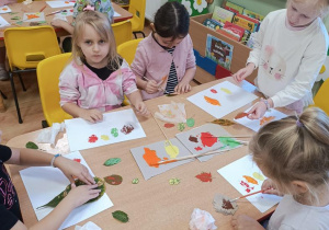 Dzieci stemplują liście tworząc z nich jesienne drzewa.