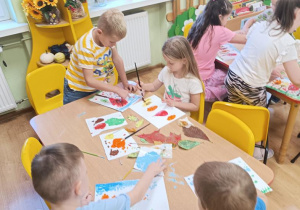 Dzieci stemplują liście tworząc z nich jesienne drzewa.