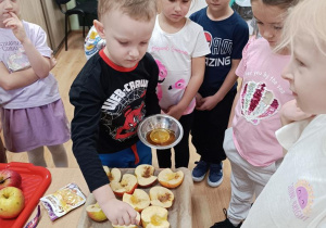 Olek polewa miodem połówki jabłek.