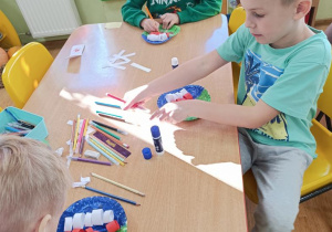 Dzieci sklejają białe i czerwone paski a następnie składają z nich flagę i rysują flamastrami z czym kojarzy się Ojczyzna.