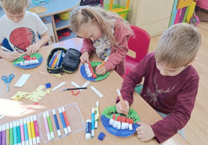 Dzieci sklejają białe i czerwone paski a następnie składają z nich flagę i rysują flamastrami z czym kojarzy się Ojczyzna.