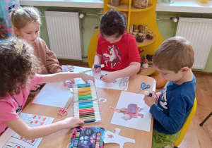 Dzieci wycinają, składają i sklejają lajkonika. W tle rysują rynek Krakowa.