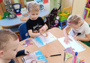 Dzieci wycinają, składają i sklejają lajkonika. W tle rysują rynek Krakowa.