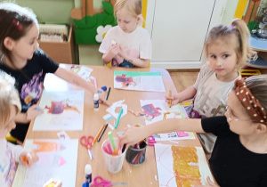 Dzieci wycinają, składają i sklejają lajkonika. W tle rysują rynek Krakowa.