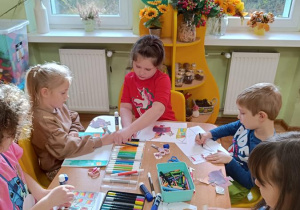 Dzieci wycinają, składają i sklejają lajkonika. W tle rysują rynek Krakowa.