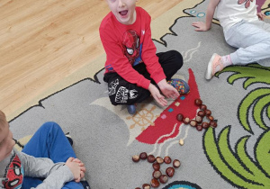 Dzieci układają z kasztanów literę a.