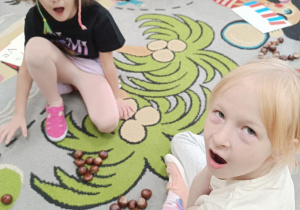 Dzieci układają z kasztanów literę a.