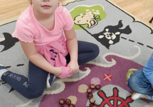 Marysia układa z kasztanów literę a.