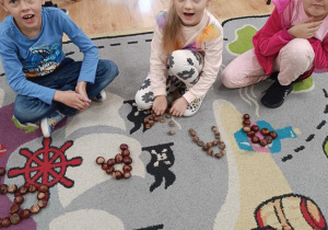 Dzieci układają z kasztanów literę a.