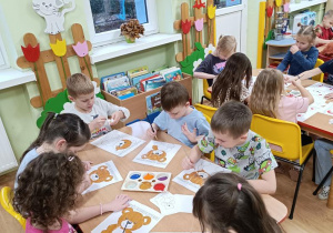 Dzieci ozdabiają misie o różnych wielkościach.