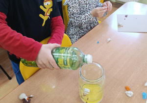 Wojtek nalewa olej do słoika z bałwanem.