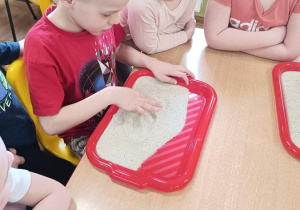 Dzieci podejmują próby pisania na piasku.