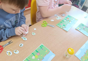 Dzieci malują kwiaty na łące i mocują na wykałaczkach owady.