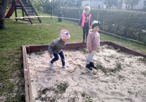 Dziewczynki skaczą do piaskownicy.