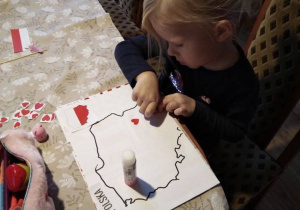 Nikola wykleja mapę Polski serduszkami w barwach narodowych.