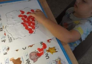 Tomek przykleja czerwone serduszko na kontur mapy Polski.