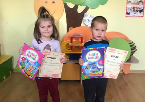 Zosia i Adaś prezentują dyplomy oraz upominki za udział w konkursie.
