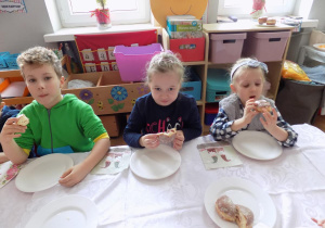 Eryk, Zosia i Nadia zajadają się pysznymi pączkami.